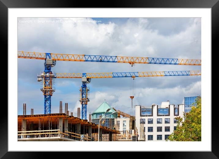 Construction site with tower cranes and the construction of a residential building against the backdrop of a cloudy sky. Framed Mounted Print by Sergii Petruk