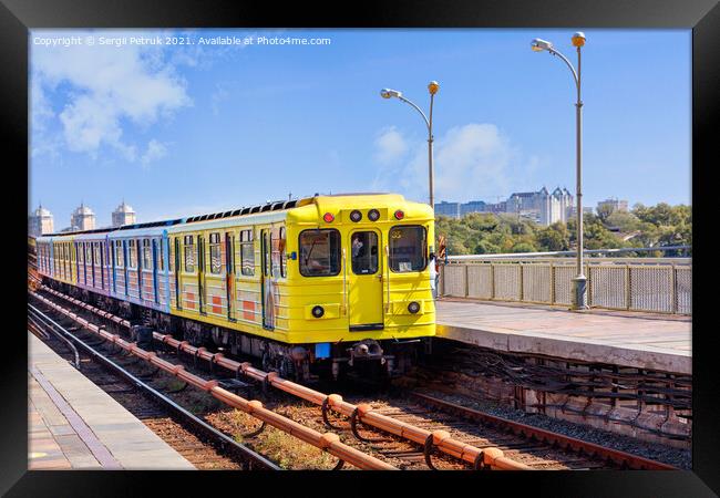 A bright yellow metro train departs from the platform and rushes along the metro bridge in Kyiv to the left side of the city. Framed Print by Sergii Petruk