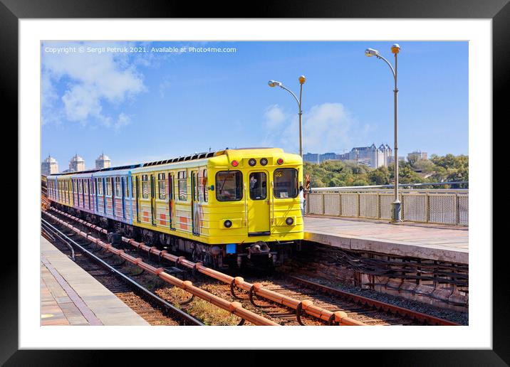 A bright yellow metro train departs from the platform and rushes along the metro bridge in Kyiv to the left side of the city. Framed Mounted Print by Sergii Petruk
