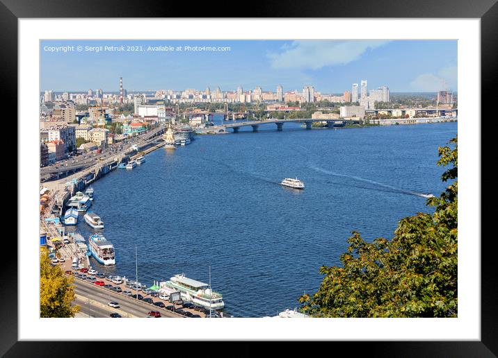 A landscape of summer Kyiv with a view of the Dnipro embankment in the old Podil district, a river station, piers, river trams and pleasure boats.30.08.20, Kyiv, Ukraine. Framed Mounted Print by Sergii Petruk