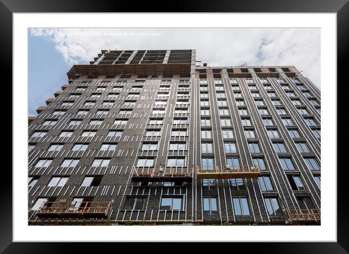 Facade of a high-rise building under construction against a blue sky. Modern architecture. Framed Mounted Print by Sergii Petruk