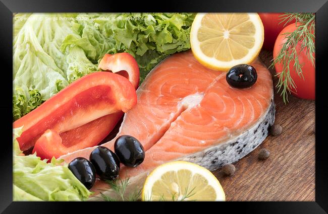 Raw salmon steak on a wooden board surrounded by vegetables, black olives and spices. Framed Print by Sergii Petruk