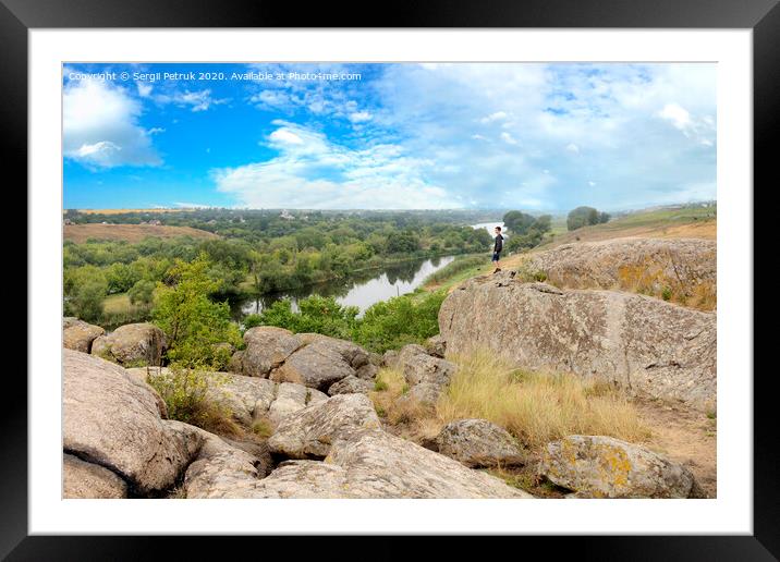 The teenager stands on top of a large stone boulder on the bank of the Southern Bug River and looks at the river below Framed Mounted Print by Sergii Petruk