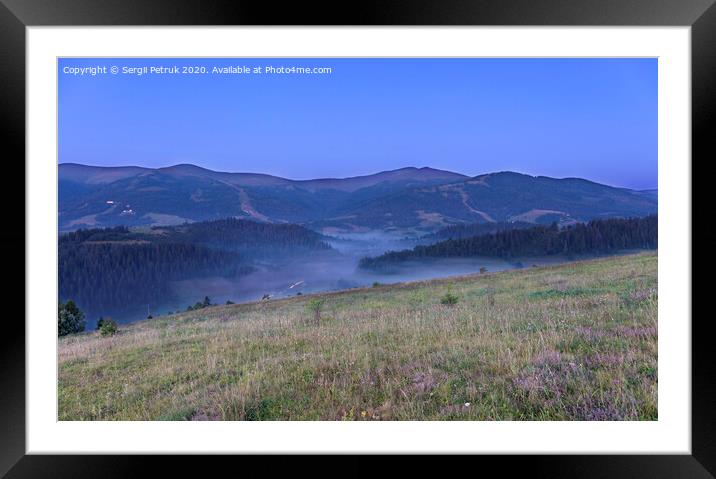 A green meadow and a gray curly fog on a hill in the background of the Carpathian Mountains in the early morning Framed Mounted Print by Sergii Petruk