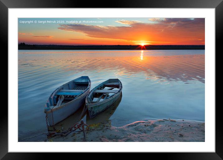 Two old blue-green boats stand on the bank of a calm river against the background of a bright rising sun Framed Mounted Print by Sergii Petruk