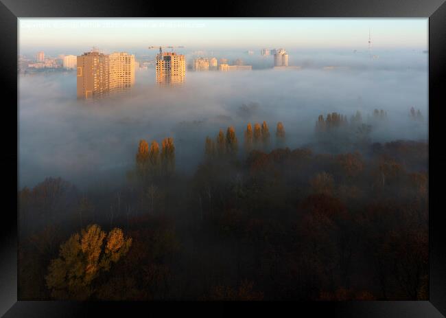 The sun's rays illuminate the morning city through the dense autumn fog Framed Print by Sergii Petruk