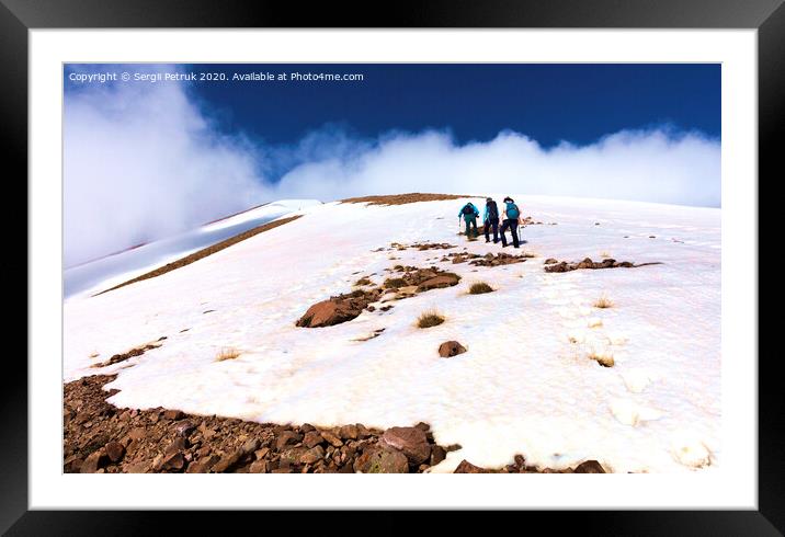 A group of tourists climbs the rocky snow-covered mountainside to its foggy summit. Framed Mounted Print by Sergii Petruk