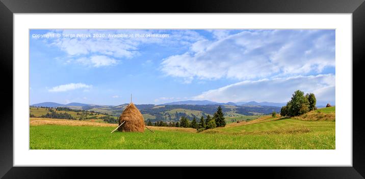 A haystack stands in a meadow against the backdrop of the Carpathian mountains and slopes. Framed Mounted Print by Sergii Petruk