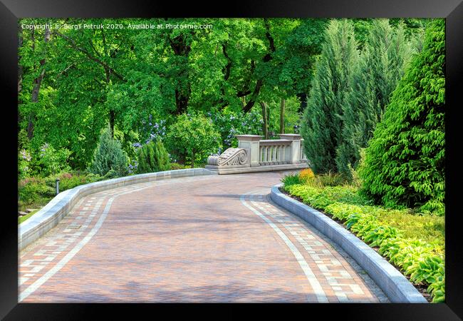 Walkway paved with tiles in a beautiful park, framed by different bushes and flowers, in soft rays of morning light. Framed Print by Sergii Petruk