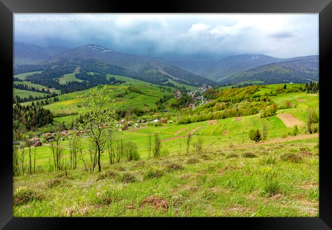 The mountain slope is covered with thick green grass against the backdrop of the picturesque landscape of the Carpathian Mountains shrouded in mist and villages in the valley. Framed Print by Sergii Petruk
