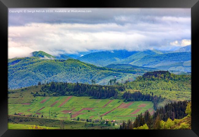 In the valley on the mountainside stretched rectangular agricultural land plots against the backdrop of the picturesque landscape of the Carpathian Mountains, shrouded in mist. Framed Print by Sergii Petruk