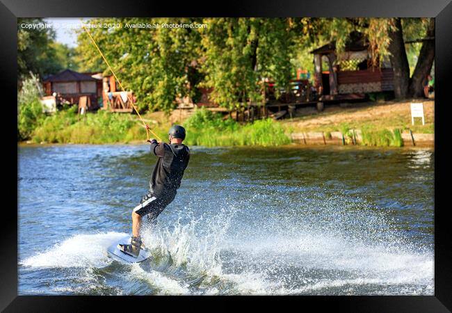 A wakeboarder rushes through the water at high speed along the green bank of the river. Framed Print by Sergii Petruk