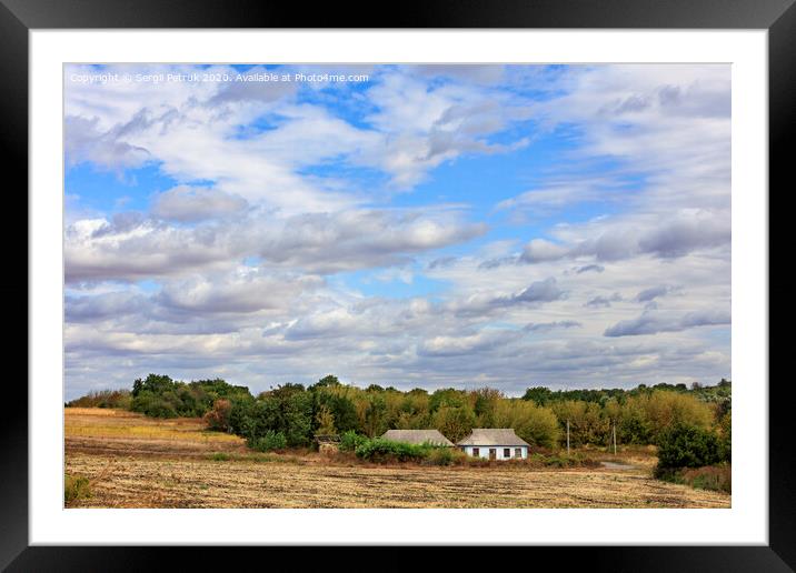 An abandoned rural house stands on the side of a rural road at the edge of a field under a cloudy sky. Framed Mounted Print by Sergii Petruk