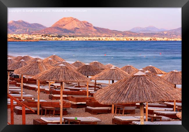 The straw tops of beach umbrellas and wooden deck chairs with mattresses on the deserted beach promenade in the rays of the evening setting sun. Framed Print by Sergii Petruk