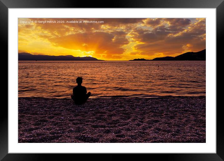 Silhouette of a teenager who sits on a pebble sea shore and watches a beautiful, vibrant sunset on the Gulf of Corinth in Greece. Framed Mounted Print by Sergii Petruk