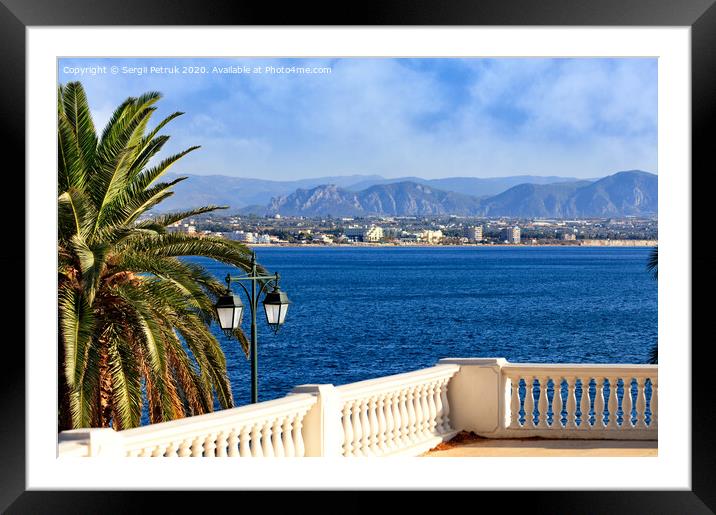 Beautiful seascape on the promenade, a street lamp under a palm tree looks at the sea, city and mountains in blur. Framed Mounted Print by Sergii Petruk