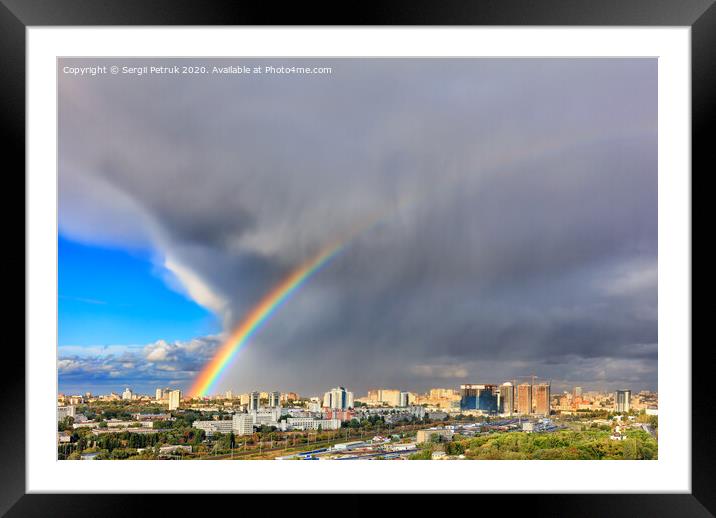 A bright rainbow in the sky above city houses after a thunderstorm separates thunderclouds from the clear sky. Framed Mounted Print by Sergii Petruk