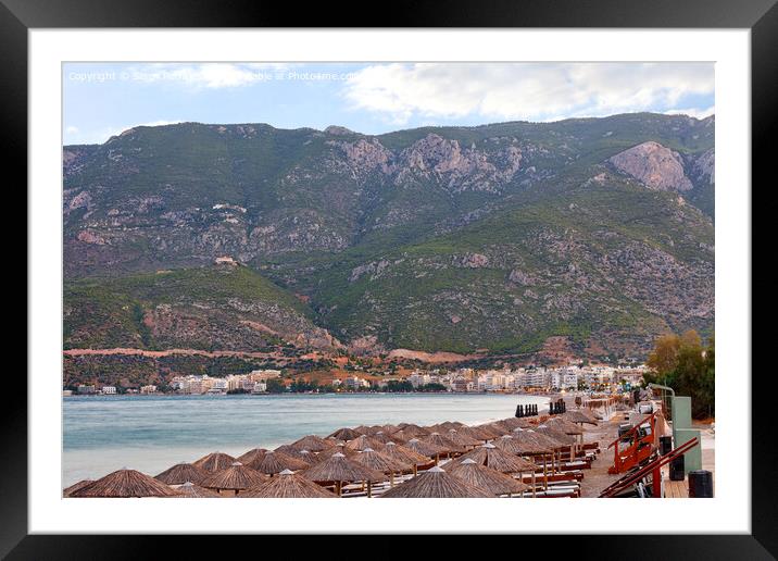 View of thatched peaks of beach umbrellas and wooden sun loungers with mattresses on the deserted waterfront of Loutraki in Greece against the backdrop of mountains in the early morning. Framed Mounted Print by Sergii Petruk