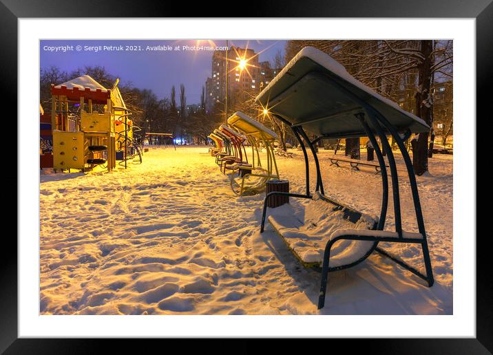 Wooden benches and a playground in the winter city evening park are covered with snow against the background of blue twilight. Framed Mounted Print by Sergii Petruk