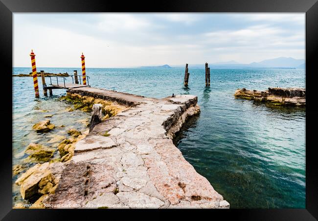 Old stone jetty at the tip of San Vigilio, on Lago di Garda with colorful mooring poles on Framed Print by Joaquin Corbalan