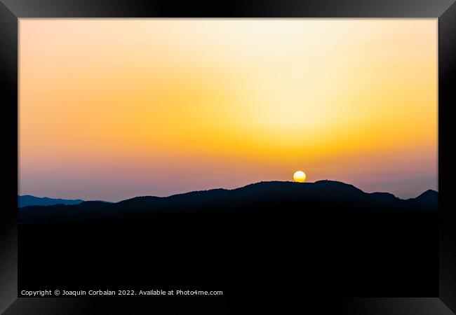 The hot sun hides behind the mountains on a summer day at dusk. Framed Print by Joaquin Corbalan