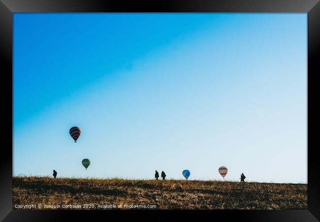 Silhouettes of tourists walking through a meadow while watching hot air balloons flying on the horizon, blue sky background, copy space, added film grain. Framed Print by Joaquin Corbalan