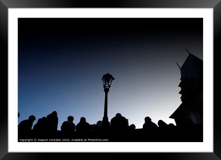 A crowd of tourists rests at dusk on a bridge, silhouetted images backlight against a streetlight. Framed Mounted Print by Joaquin Corbalan