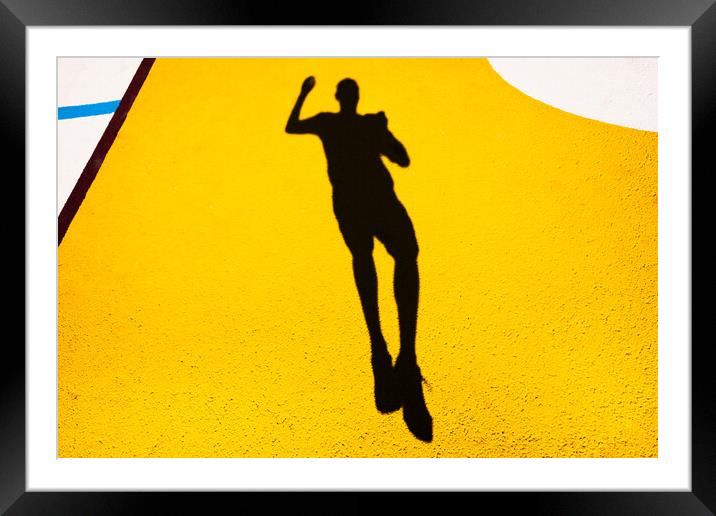 Shadow and silhouette of a man jumping on a yellow painted floor. Framed Mounted Print by Joaquin Corbalan