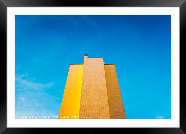 High brick building, warm and yellow at sunset, with the background of an intense blue sky and copy space, minimalist architecture. Framed Mounted Print by Joaquin Corbalan