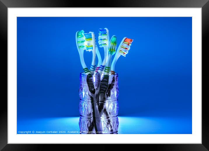Many new plastic toothbrushes inside a glass, isolated on striking blue background, with copy space. Framed Mounted Print by Joaquin Corbalan