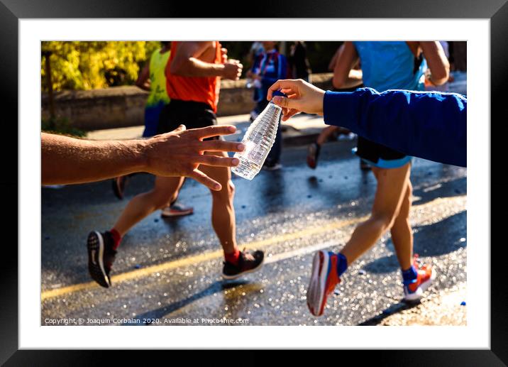 Runner collects a bottle of water to hydrate during a workout. Framed Mounted Print by Joaquin Corbalan