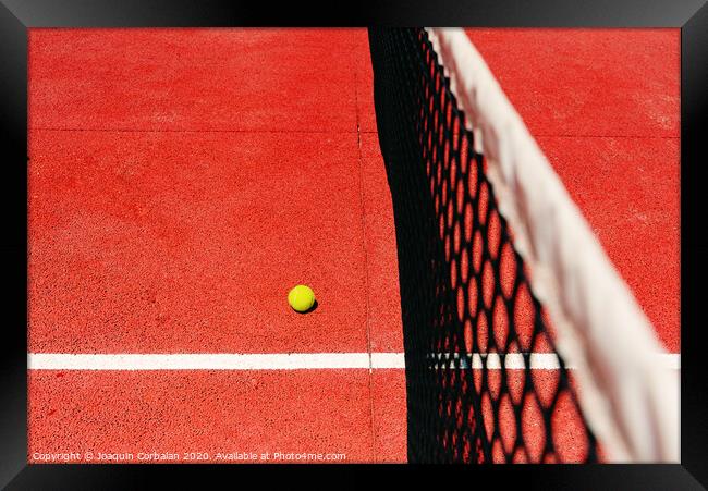 A tennis ball on the textured floor of a red court near the net after losing a match point. Framed Print by Joaquin Corbalan