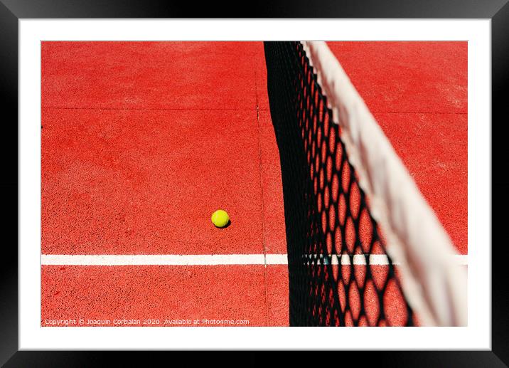 A tennis ball on the textured floor of a red court near the net after losing a match point. Framed Mounted Print by Joaquin Corbalan
