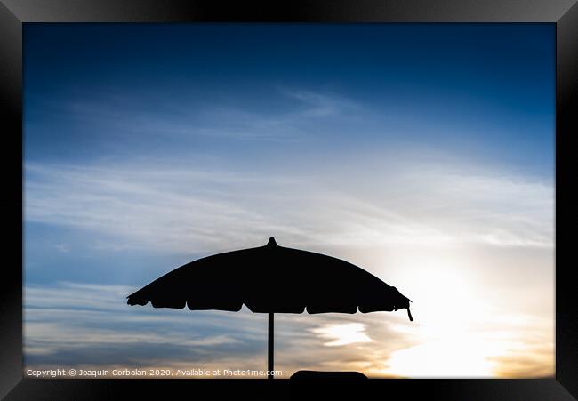 Silhouette of beach umbrella against backlight on a hot summer day. Framed Print by Joaquin Corbalan