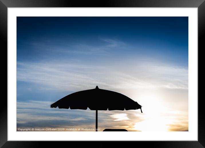 Silhouette of beach umbrella against backlight on a hot summer day. Framed Mounted Print by Joaquin Corbalan