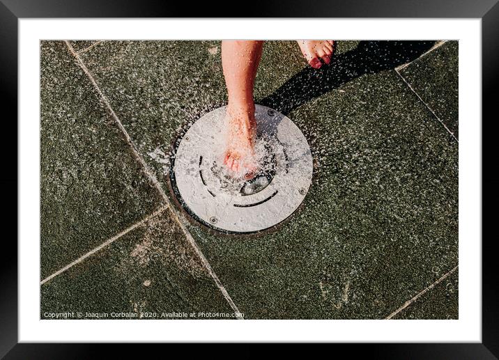 Young barefoot boy running through squirting water in a pool in a spa. Framed Mounted Print by Joaquin Corbalan