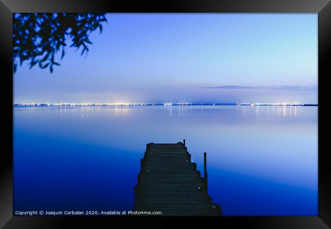 Pier on a lake at sunset with calm water and reflections of relaxing lights. Framed Print by Joaquin Corbalan
