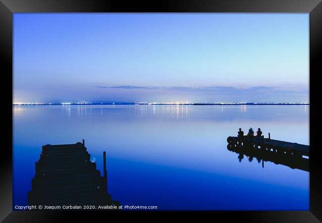 People resting relaxed on a pier on a lake at sunset with calm water Framed Print by Joaquin Corbalan