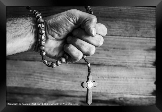 Hand of a religious person holds a Christian rosary during his prayers, unfocused background of woods in black and white. Framed Print by Joaquin Corbalan
