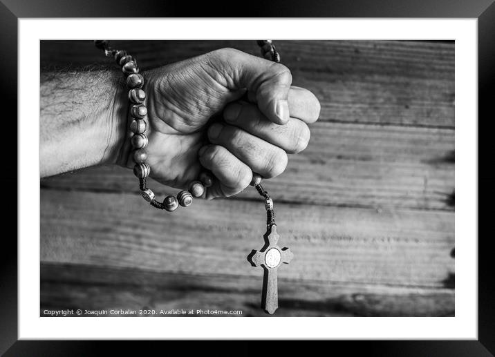 Hand of a religious person holds a Christian rosary during his prayers, unfocused background of woods in black and white. Framed Mounted Print by Joaquin Corbalan