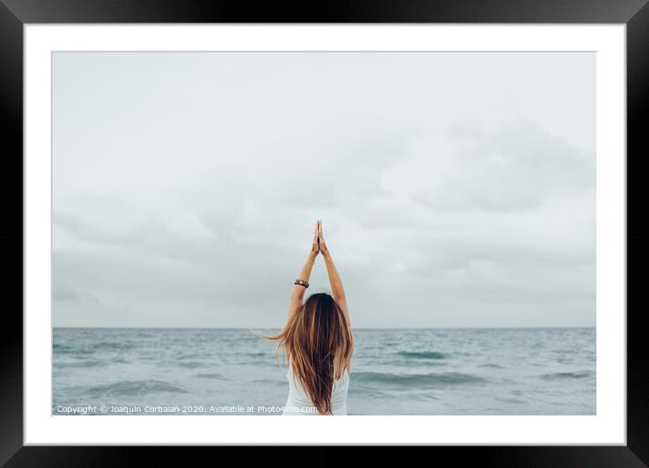 A woman relaxes in front of the sea with her hands up, unfocused background. Framed Mounted Print by Joaquin Corbalan