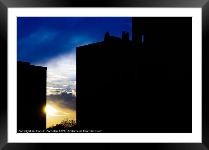 Sunset silhouette in a city with the warm sun behind buildings. Framed Mounted Print by Joaquin Corbalan