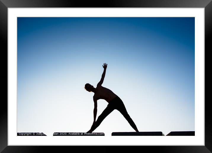 Silhouette of a man practicing yoga, isolated against the blue sky. Framed Mounted Print by Joaquin Corbalan