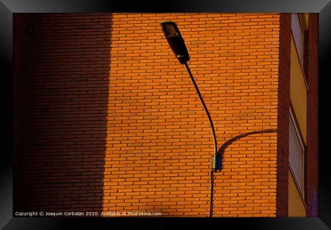 A deep red brick wall supports a lamppost, contrasting and bright colors. Framed Print by Joaquin Corbalan