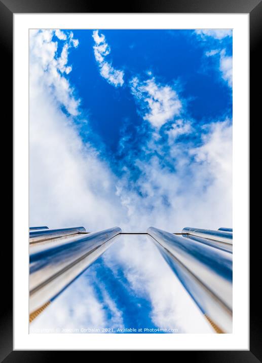 Fence with tall metal bars pointing to the blue sky with perspec Framed Mounted Print by Joaquin Corbalan