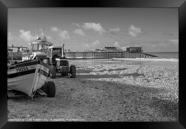Black and white vintage photo of fishing boats and equipment on Cromer beach on the North Norfolk Coast. In the distance is the Victorian era pier Framed Print by Chris Yaxley