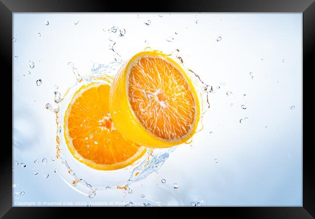 Two halves of orange fruit splashing into clear water. Framed Print by Przemek Iciak