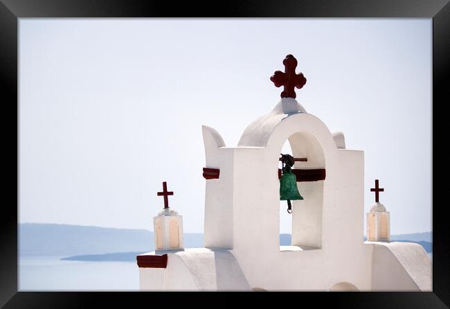 A tower top of a church with cross sign and bells architecture located in oia village in one of Cycladic island in Santorini, Greece against sea. Framed Print by Arpan Bhatia
