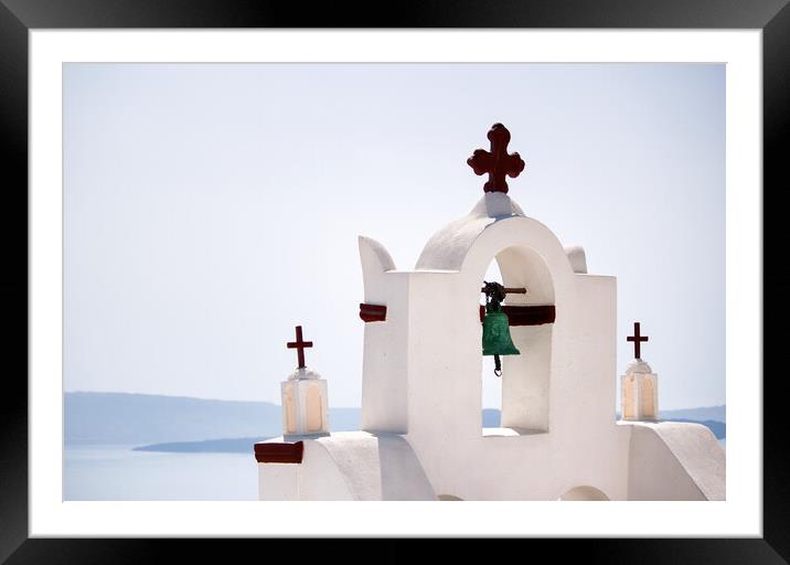 A tower top of a church with cross sign and bells architecture located in oia village in one of Cycladic island in Santorini, Greece against sea. Framed Mounted Print by Arpan Bhatia