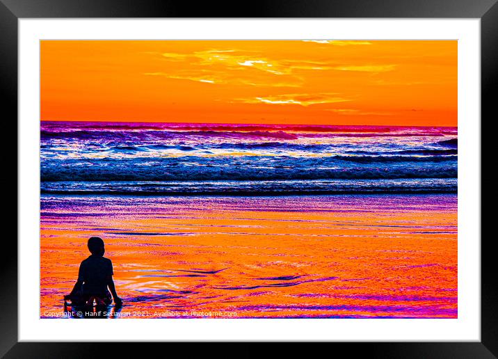 A young boy enjoys the sunset at a sand beach. Framed Mounted Print by Hanif Setiawan